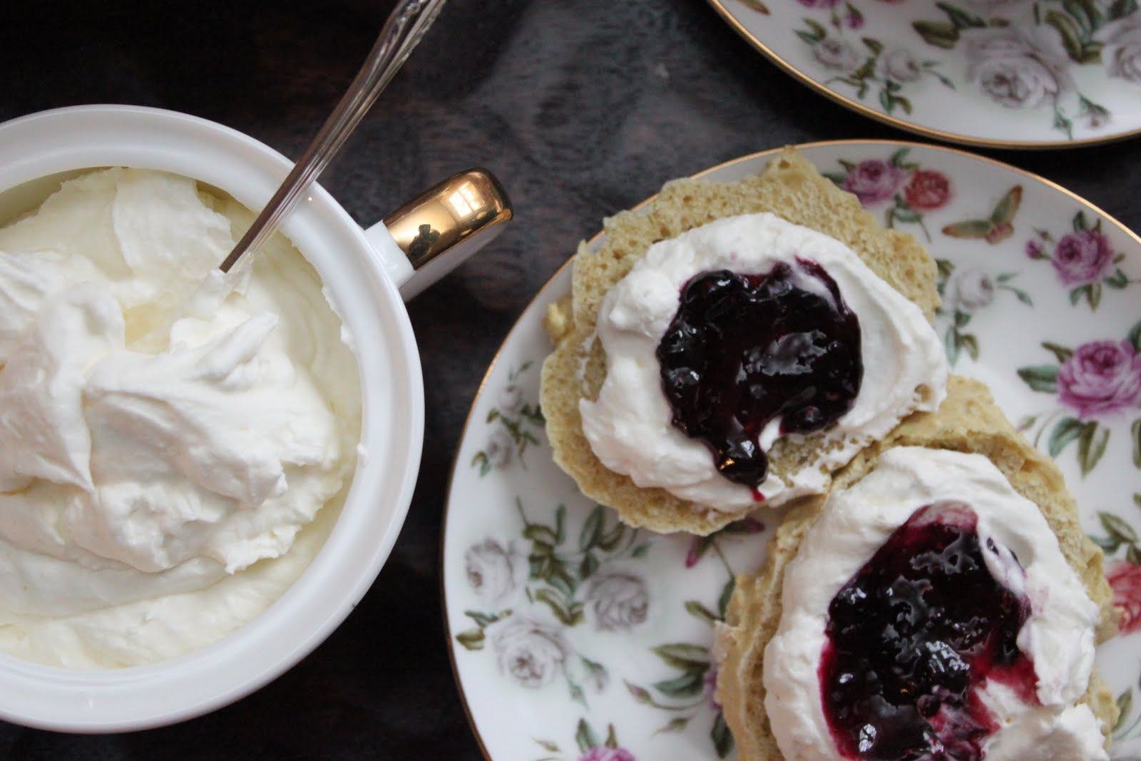 Two scones topped with cream and blueberry jam on a floral plate.