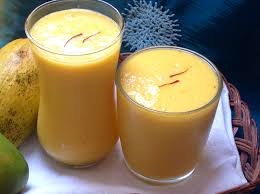 Two glasses filled with thick mango juice, garnished with cardamom pods.