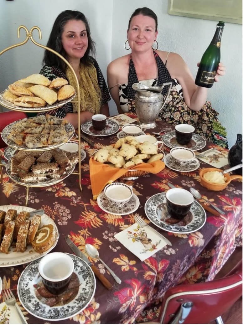 Two women enjoying tea with assorted pastries and champagne.