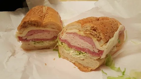A sliced sandwich with layers of ham and lettuce on a crusty roll.