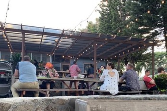 People gathered outdoors at picnic tables under string lights in the evening.