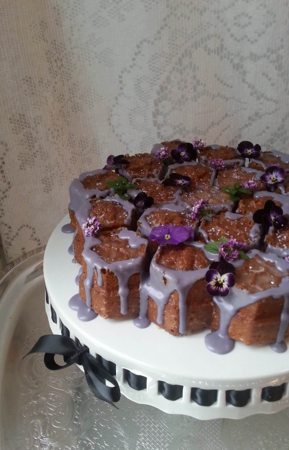 A beautifully decorated cake with purple flowers and white glaze.