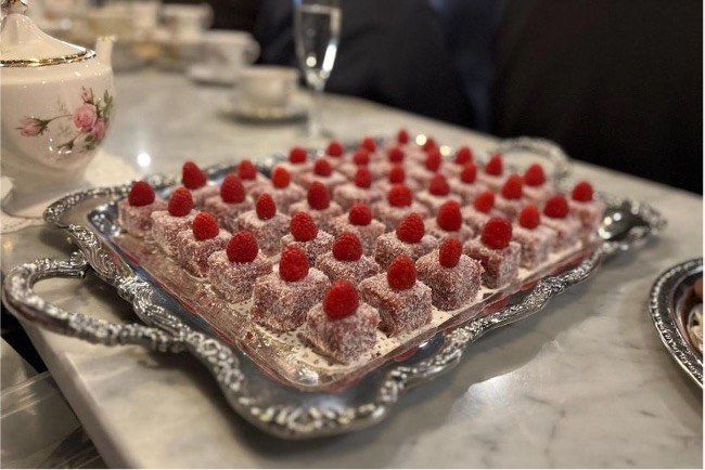 Raspberry-topped desserts on ornate silver tray.
