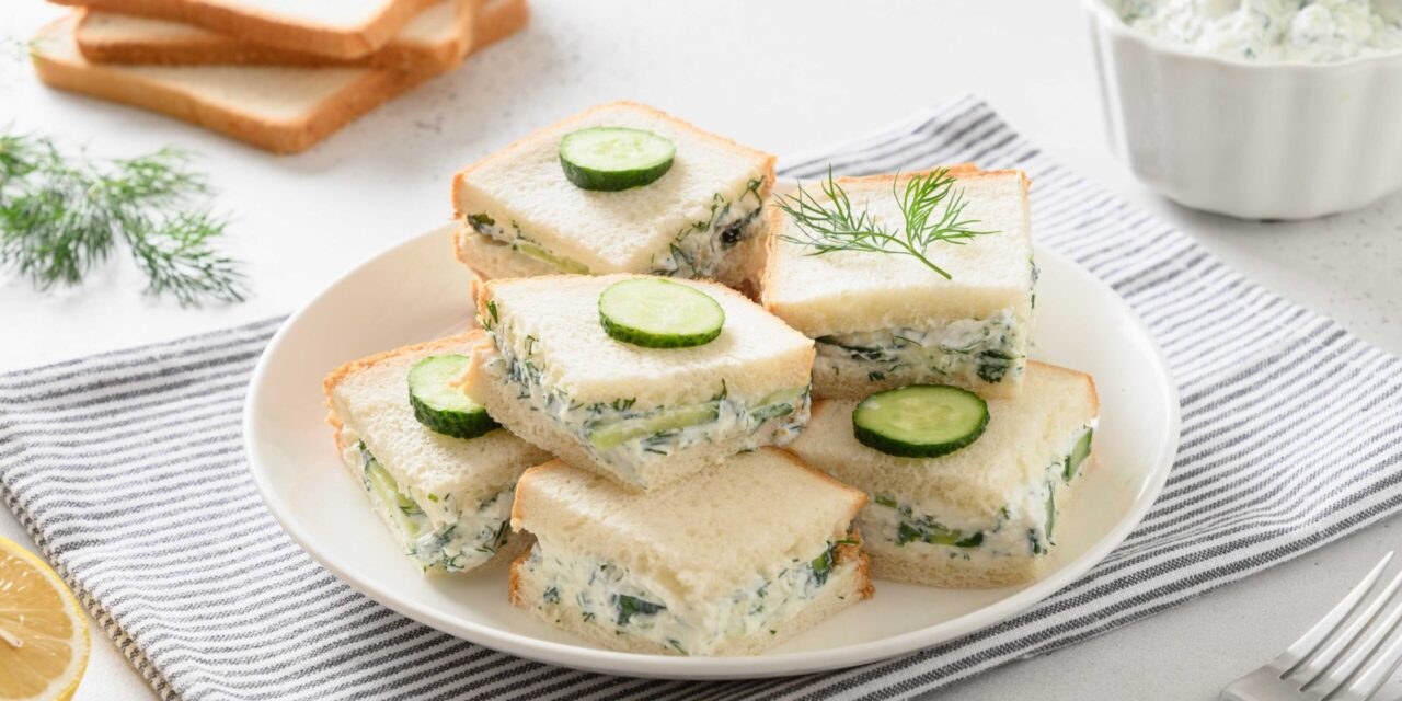 Cucumber tea sandwiches garnished with dill on a white plate.
