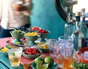 A colorful display of fresh fruits and drinks on a table with a blurry person in the background.