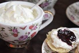 A floral teacup filled with cream beside a biscuit topped with cream and jam.