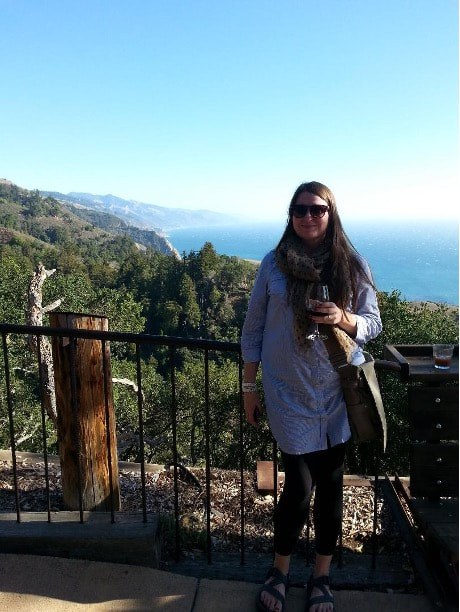 Person enjoying a scenic view of mountains and sea from a wooden fence.
