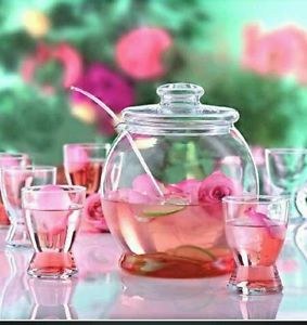 Glass teapot and cups with rose tea on a pink table