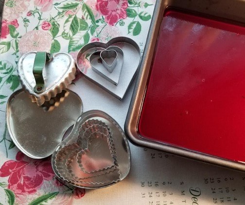 Heart-shaped cookie cutters and a tray with red liquid for baking.