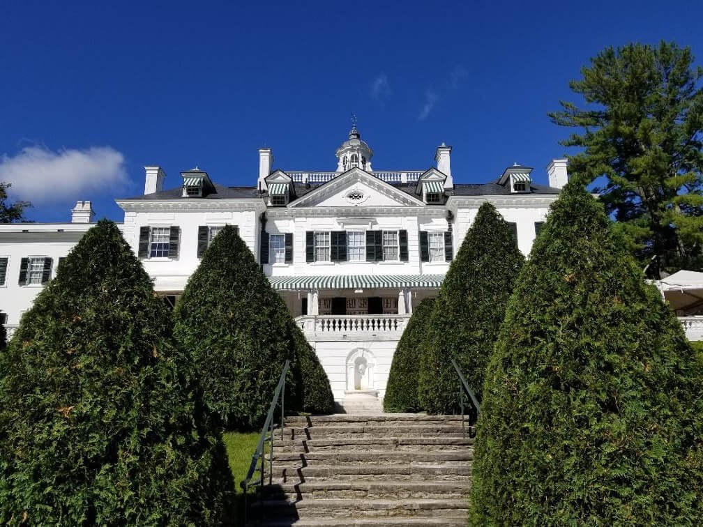 Elegant white mansion with manicured shrubs under a clear blue sky.