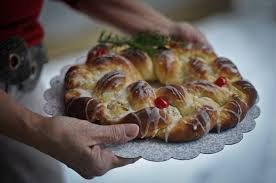 A freshly baked, golden-brown bread with cherry toppings held on a white lace plate.
