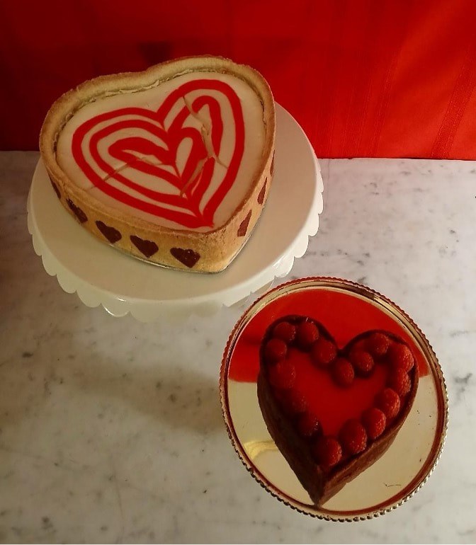 Heart-shaped cakes with red and chocolate decorations on a white surface.