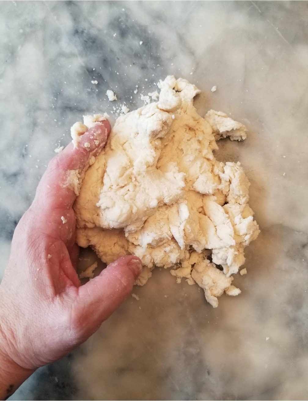 Hand mixing dough on a marble surface.