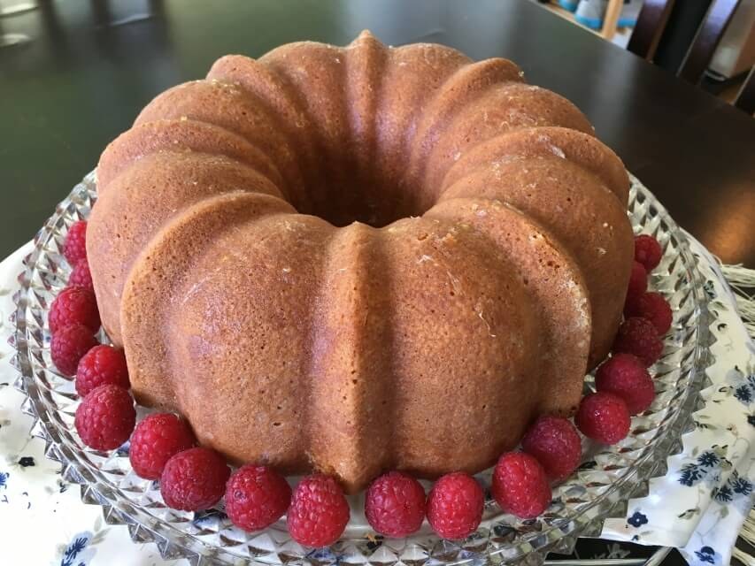 A bundt cake surrounded by fresh raspberries on a glass plate.