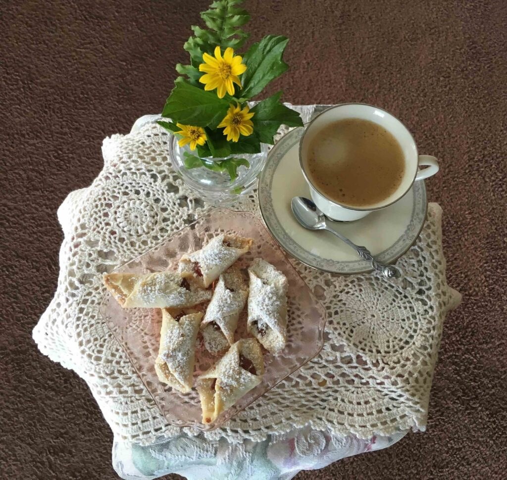 A cup of coffee with sugar cubes and a small flower vase on a lace-covered table.