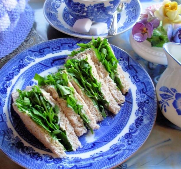 Tea sandwiches with leafy greens on a blue and white plate.