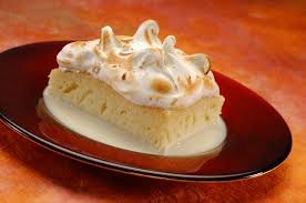 Slice of lemon meringue pie with toasted peaks on a brown plate.