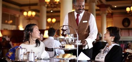 A waiter serves afternoon tea to a smiling woman in a cozy restaurant.