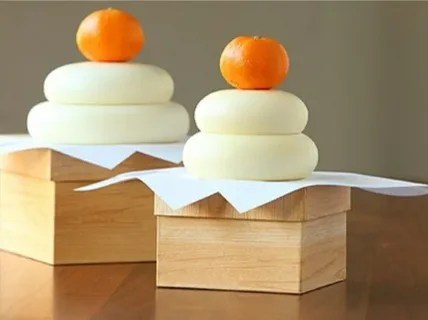 Traditional Japanese kagami mochi with mandarin oranges on wooden stands.
