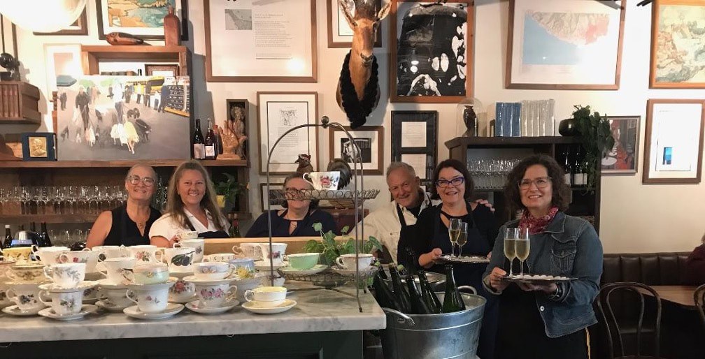 Four women enjoying wine and conversation in a cozy, art-filled room.