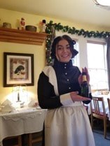 Woman dressed in historical attire holding a bottle in a decorated room.