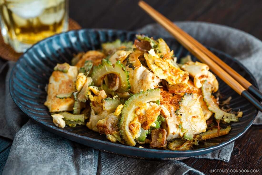 Stir-fried tofu with vegetables in a blue bowl with chopsticks.