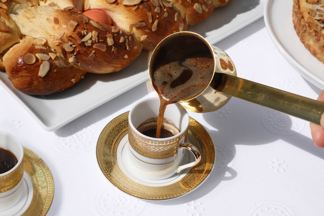 Pouring Turkish coffee into a small cup beside pastries.