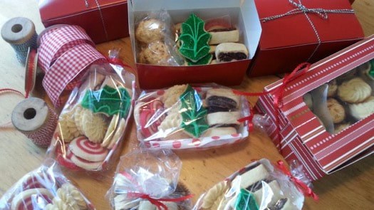 Assorted Christmas cookies decorated with green holly leaves, packed in festive boxes and bags.