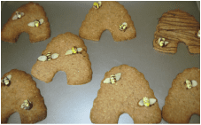 Honeybee-shaped cookies decorated with bee candies on a baking tray.