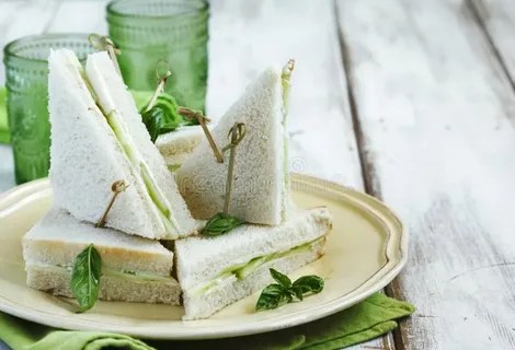 Fresh cucumber tea sandwiches stacked on a plate with herbs.
