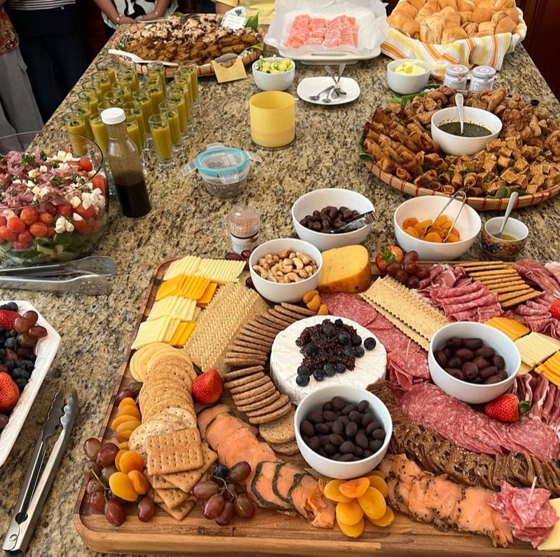 A charcuterie board with meats, cheeses, nuts, and dips on a table with snacks.