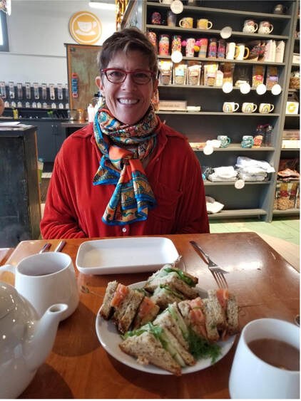 Smiling woman enjoying a sandwich and coffee at a cozy café.