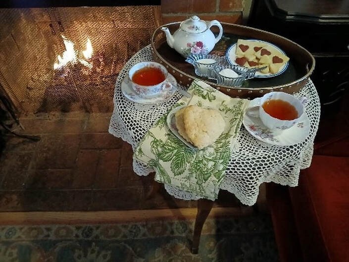 Tea set with scones and jam on a lace-covered wooden table.