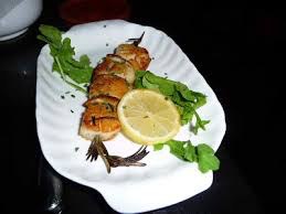 Grilled fish garnished with lemon slices and fresh greens on a white platter.