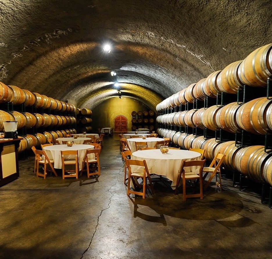 Wine cellar with barrels and tables set for tasting.