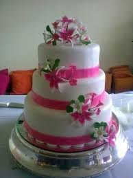 Elegant three-tier white wedding cake with pink ribbons and floral decorations.