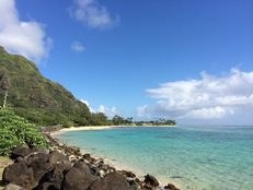 A serene beach with clear turquoise water and rocky shoreline under a blue sky.
