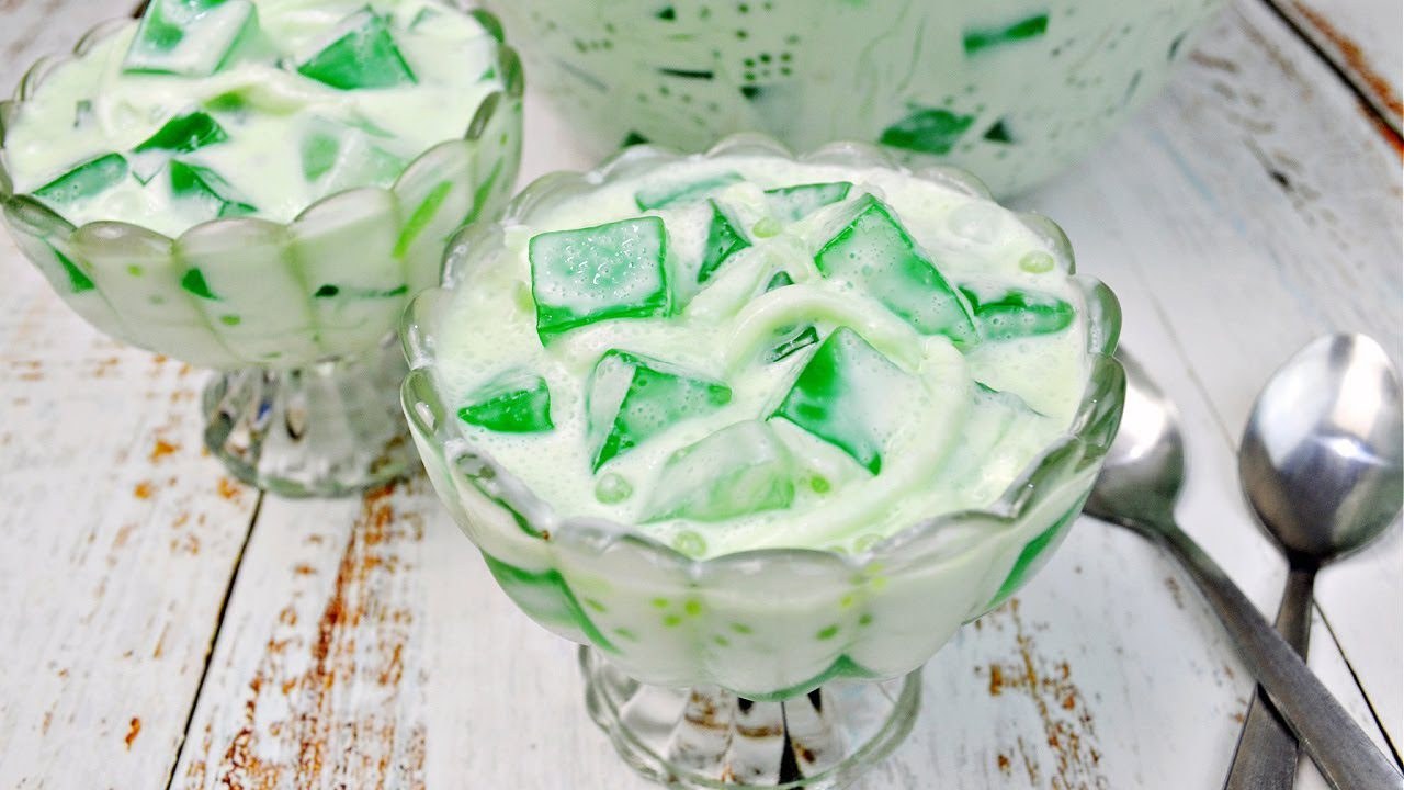 A dessert bowl filled with green jelly cubes in creamy white sauce.