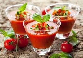 Three glasses of fresh gazpacho soup garnished with herbs.