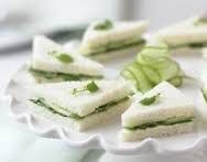 Cucumber tea sandwiches garnished with herbs on a white plate.