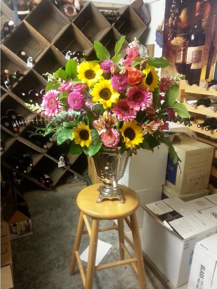 A vibrant bouquet of sunflowers and pink flowers in a vase on a wooden stool.