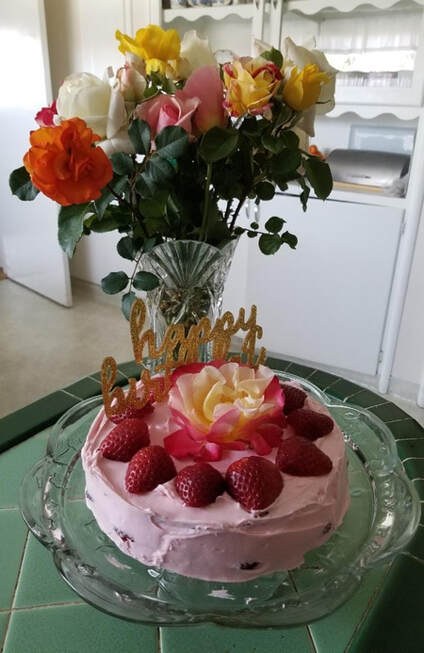 Pink birthday cake with raspberries and a gold "Happy Birthday" topper.