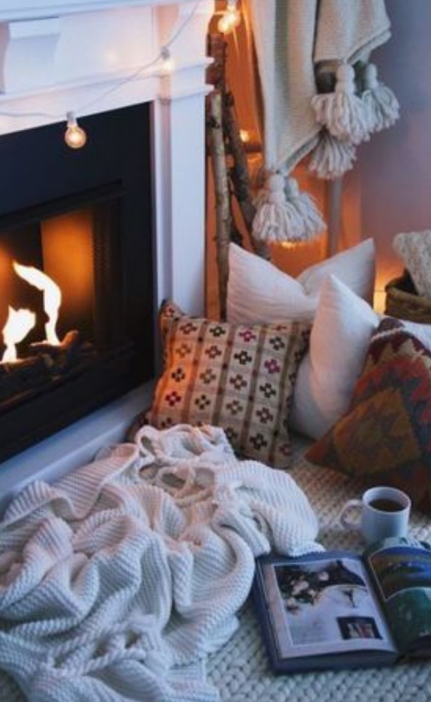 Cozy fireplace scene with pillows, blanket, and coffee cup.