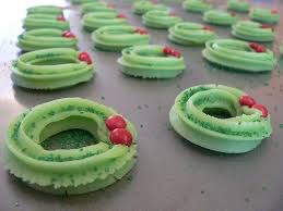 Green piped cookie dough rings with red decorations on a baking sheet.