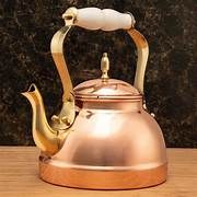 A vintage copper kettle with a white handle on a wooden surface.