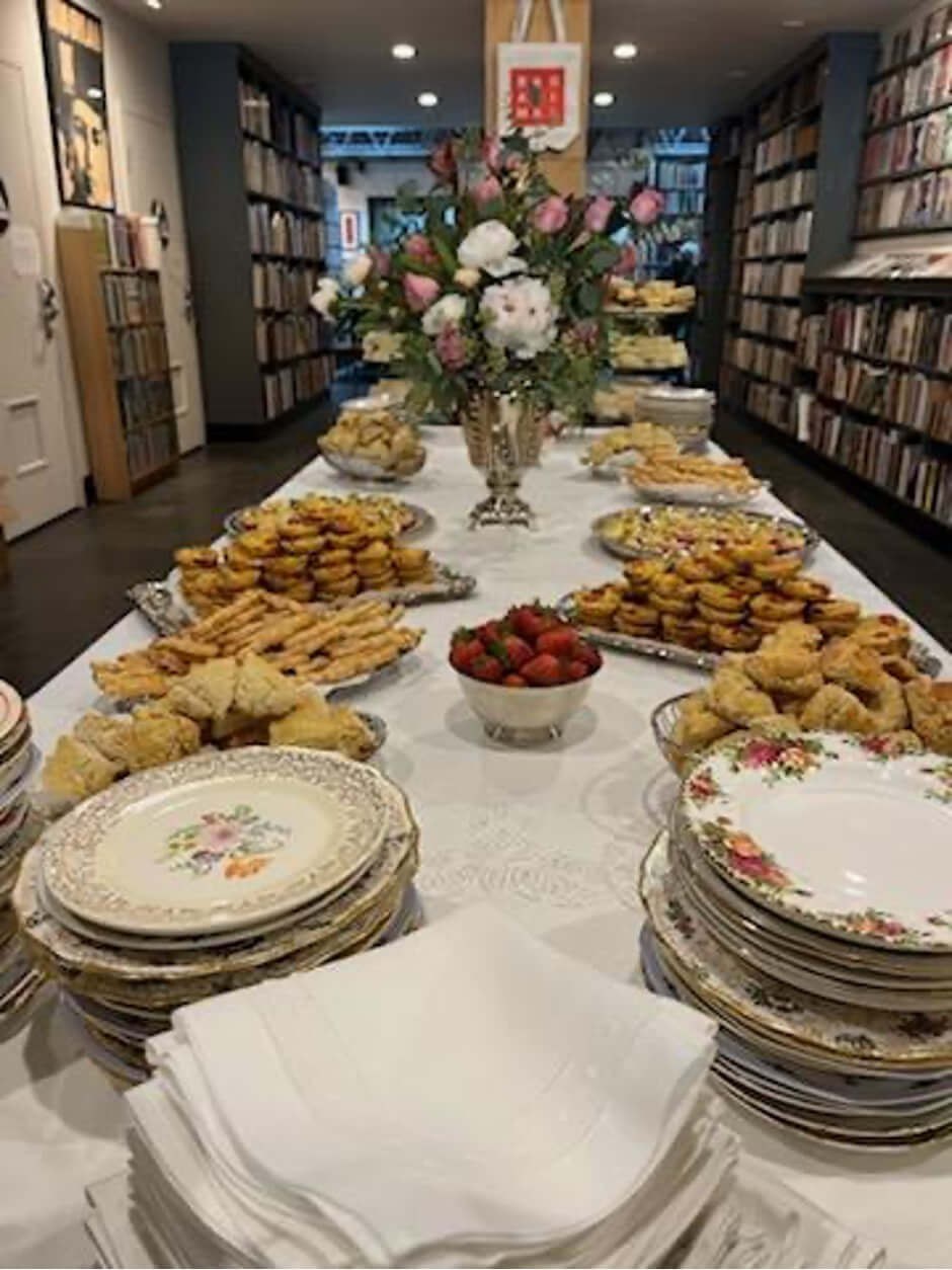 Elegant buffet setup with pastries and fresh flowers in a cozy bookshop.