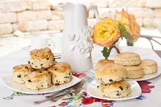 Plate of scones with raisins and a vase of yellow roses on a table.