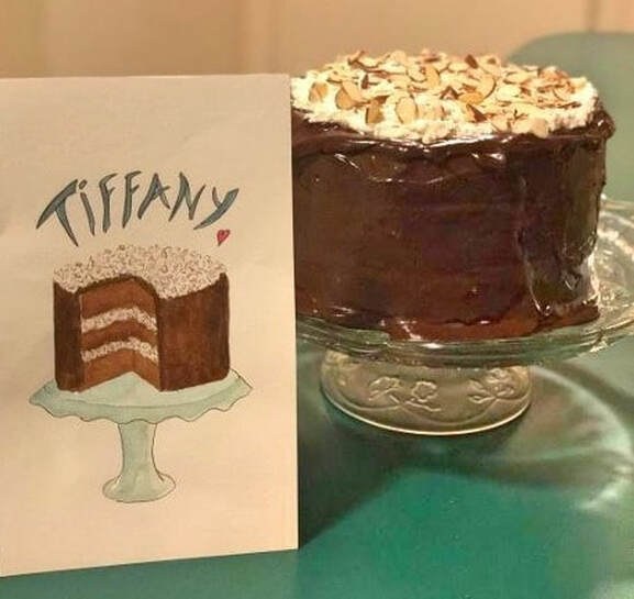A chocolate layer cake with a card showing its illustrated design.