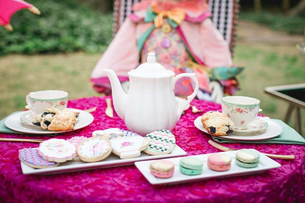 Elegant tea party setup with teapot and assorted treats on a vibrant pink tablecloth.