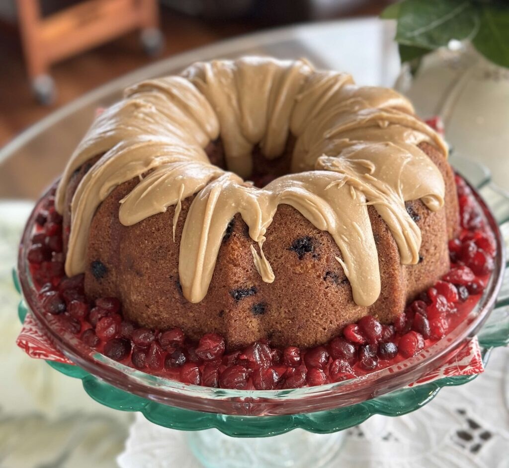 A bundt cake with caramel glaze and pomegranate seeds on a glass stand.